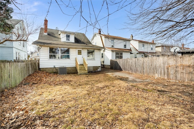 rear view of house with central AC unit, a fenced backyard, a chimney, and entry steps