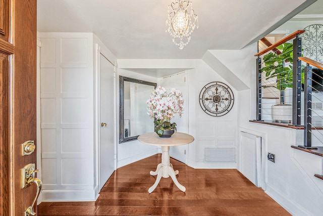 entryway featuring visible vents, a decorative wall, wood finished floors, and a chandelier