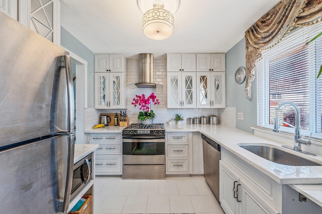 kitchen featuring stainless steel appliances, light countertops, wall chimney range hood, and a sink