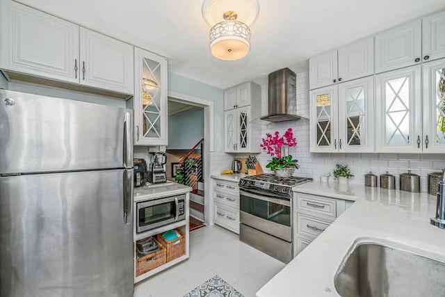 kitchen featuring stainless steel appliances, wall chimney exhaust hood, decorative backsplash, and white cabinetry