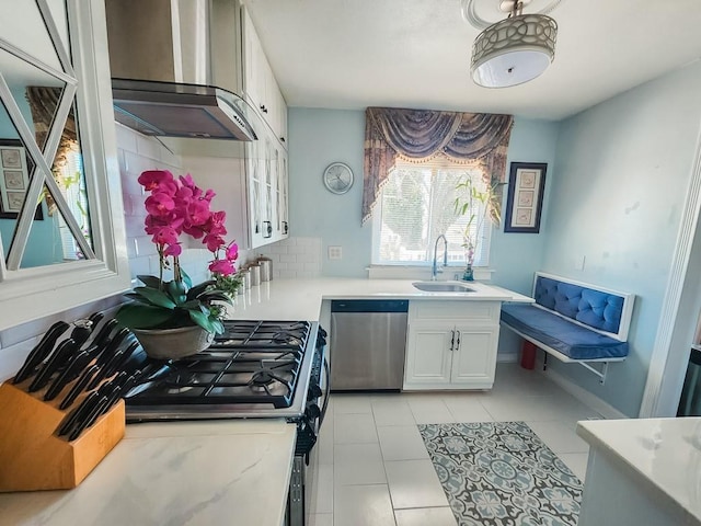 kitchen featuring wall chimney range hood, dishwasher, light countertops, decorative backsplash, and a sink