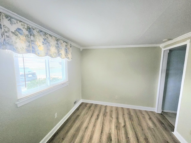 empty room with visible vents, baseboards, wood finished floors, and crown molding