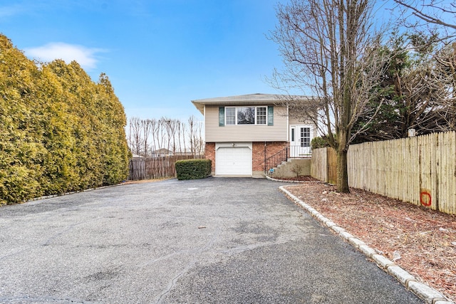 view of front of home with aphalt driveway, an attached garage, fence, and brick siding