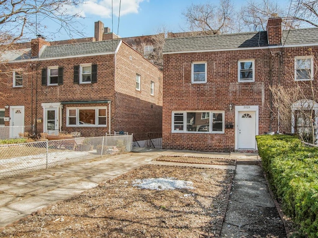 rear view of house with a fenced front yard, brick siding, a chimney, and a shingled roof