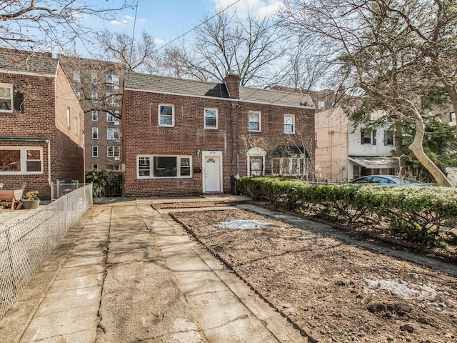 view of front facade with brick siding, a chimney, and fence