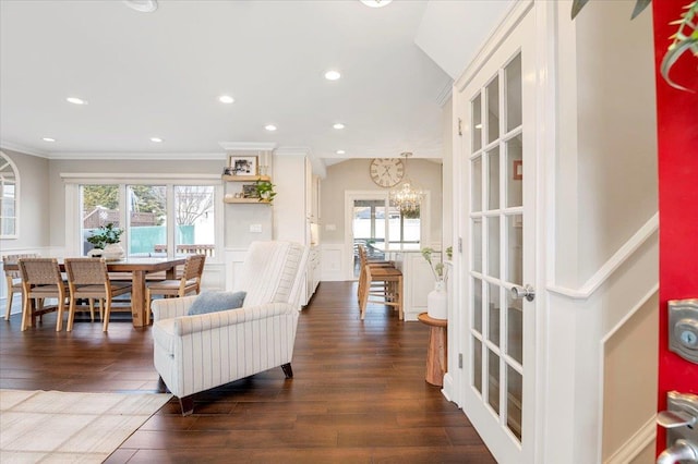 living room with dark wood finished floors, ornamental molding, wainscoting, a decorative wall, and a chandelier