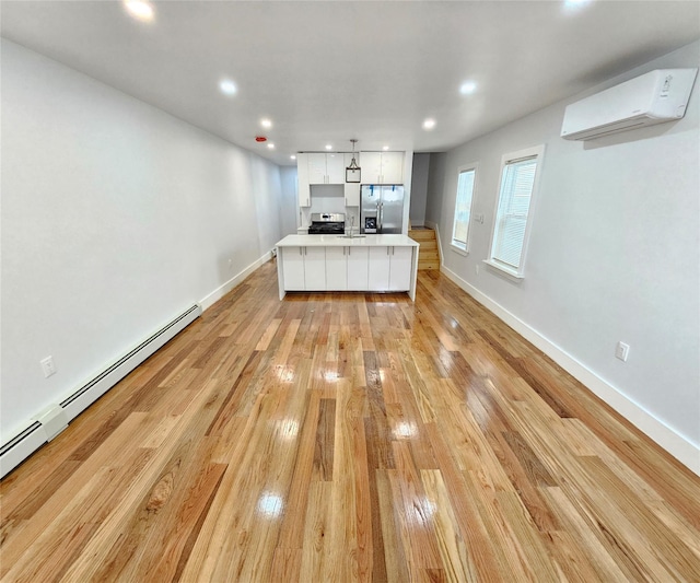 kitchen with an AC wall unit, white cabinetry, stainless steel appliances, light wood-style floors, and baseboard heating