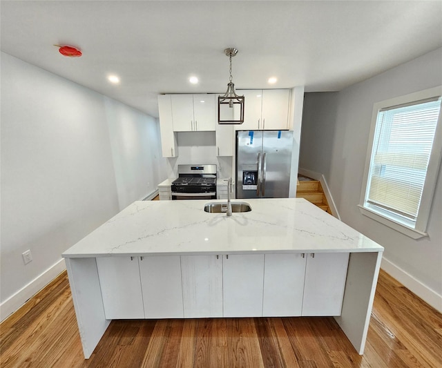 kitchen featuring pendant lighting, wood finished floors, white cabinets, stainless steel appliances, and a sink