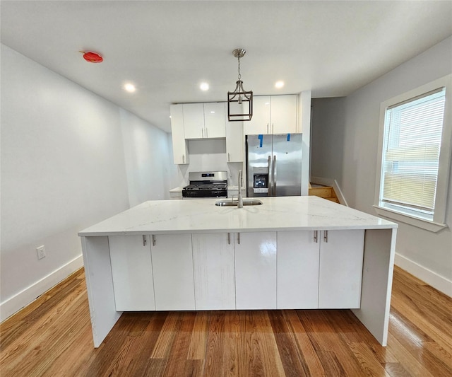 kitchen featuring a sink, light stone counters, wood finished floors, appliances with stainless steel finishes, and a large island with sink