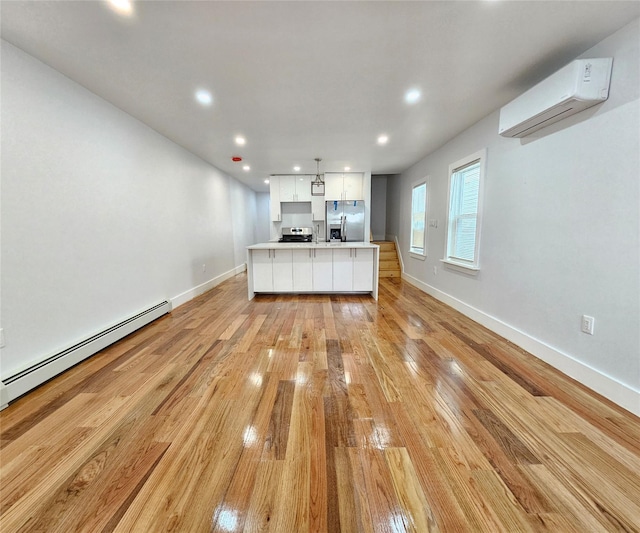 kitchen with light wood-type flooring, baseboard heating, stainless steel appliances, white cabinetry, and a wall mounted AC