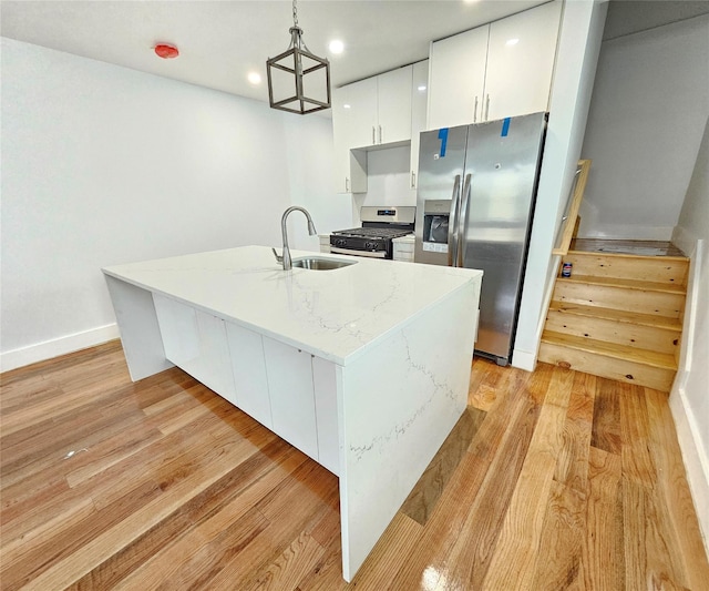 kitchen with light stone counters, appliances with stainless steel finishes, light wood-style floors, white cabinetry, and a sink