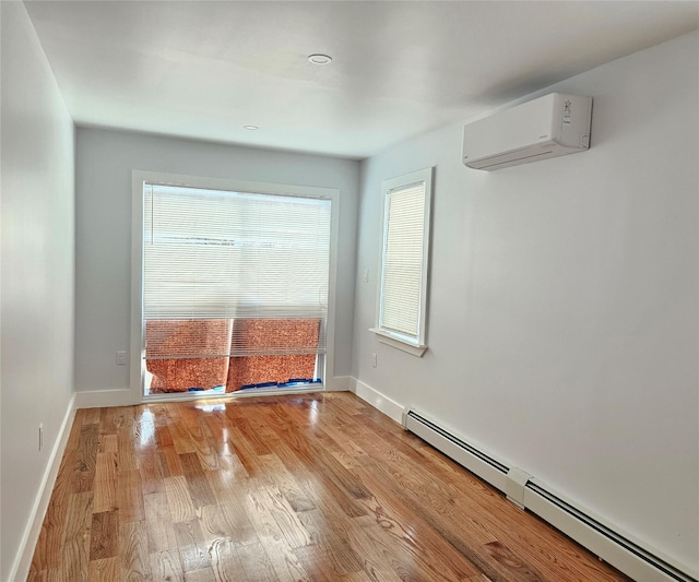 unfurnished room featuring a baseboard heating unit, a wall unit AC, baseboards, and light wood finished floors