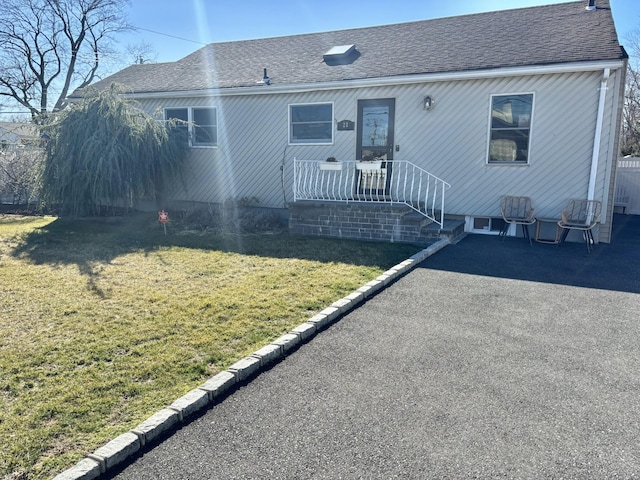 view of front of home featuring a patio, a shingled roof, and a front lawn