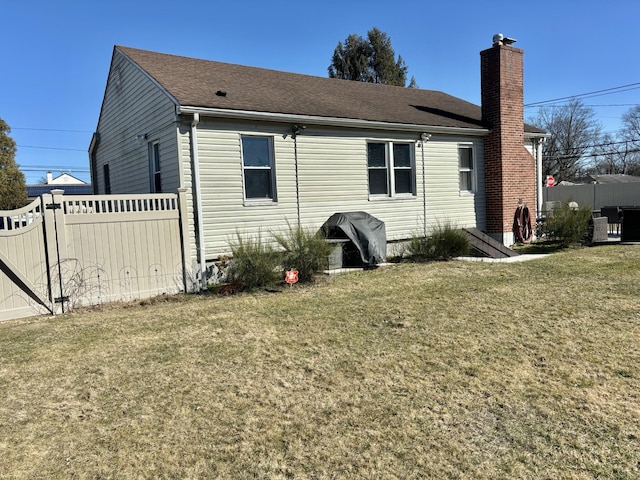 rear view of house featuring fence, a lawn, roof with shingles, and a chimney