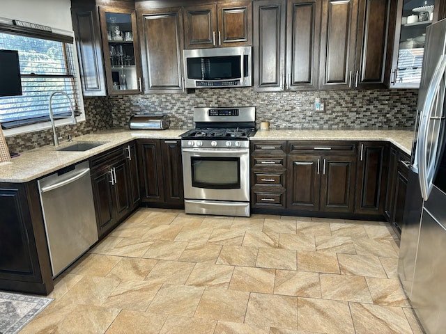 kitchen featuring dark brown cabinetry, light stone counters, decorative backsplash, appliances with stainless steel finishes, and a sink