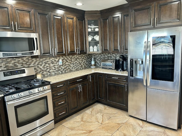 kitchen with light stone counters, a toaster, dark brown cabinetry, appliances with stainless steel finishes, and backsplash