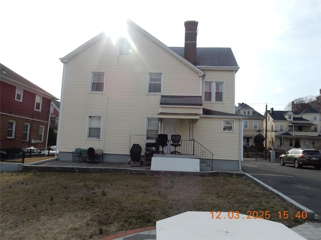 rear view of house with a patio area, a lawn, and a chimney