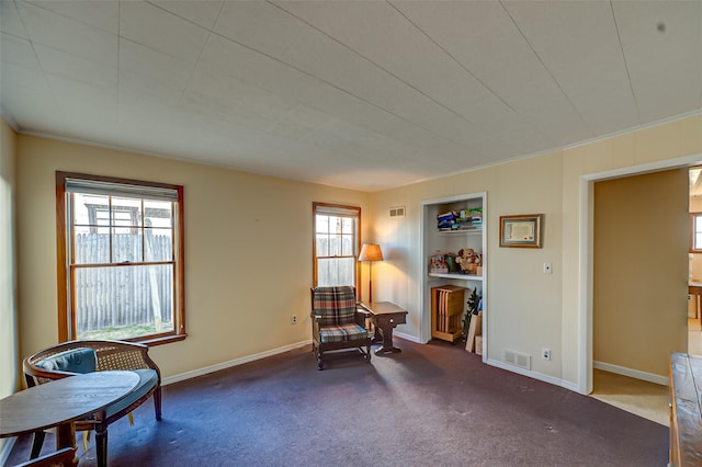 living area featuring visible vents, built in shelves, carpet, and baseboards