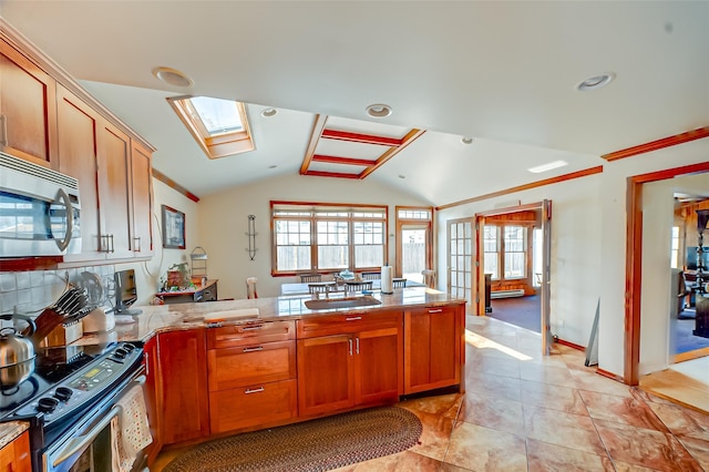 kitchen featuring brown cabinetry, a peninsula, ornamental molding, appliances with stainless steel finishes, and lofted ceiling with skylight