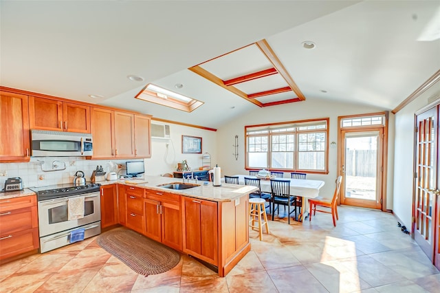 kitchen with lofted ceiling, decorative backsplash, appliances with stainless steel finishes, a peninsula, and a sink