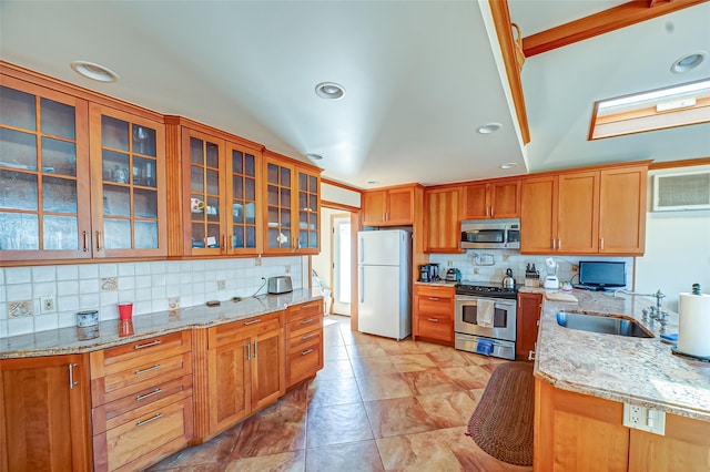 kitchen featuring a sink, light stone counters, tasteful backsplash, appliances with stainless steel finishes, and glass insert cabinets