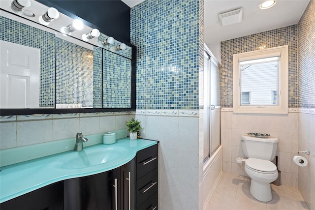 bathroom with vanity, bath / shower combo with glass door, tile walls, toilet, and tile patterned floors