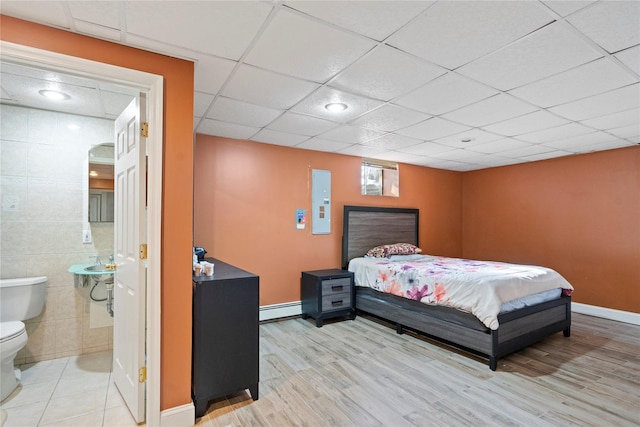 bedroom with light wood finished floors, connected bathroom, baseboards, tile walls, and a baseboard radiator