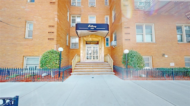 view of exterior entry featuring brick siding and fence