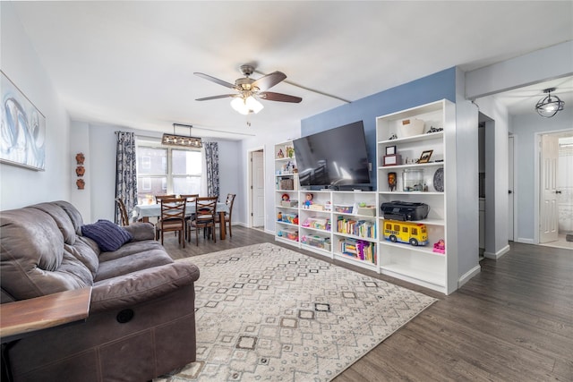 living room featuring built in shelves, baseboards, a ceiling fan, and wood finished floors