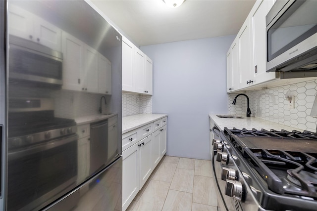 kitchen featuring white cabinets, light stone counters, appliances with stainless steel finishes, and a sink