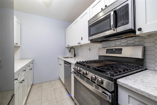 kitchen with light stone countertops, a sink, stainless steel appliances, white cabinets, and backsplash