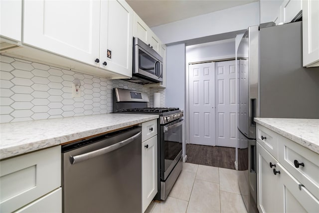 kitchen featuring backsplash, light stone counters, appliances with stainless steel finishes, light tile patterned flooring, and white cabinetry