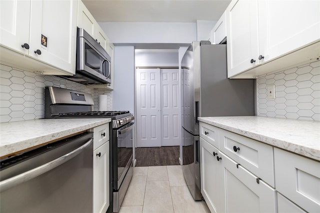 kitchen with light tile patterned floors, light stone countertops, white cabinets, appliances with stainless steel finishes, and tasteful backsplash