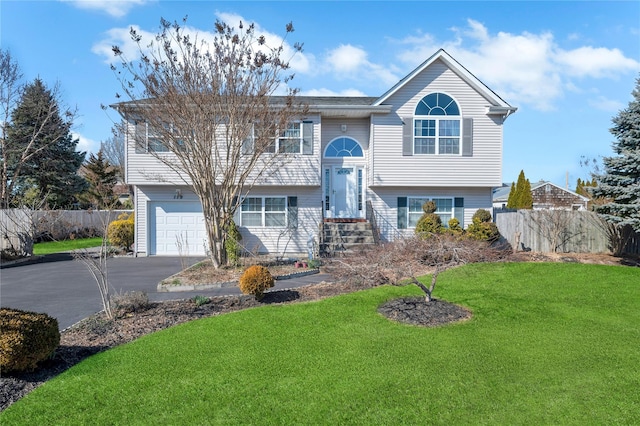 bi-level home featuring aphalt driveway, a garage, a front yard, and fence