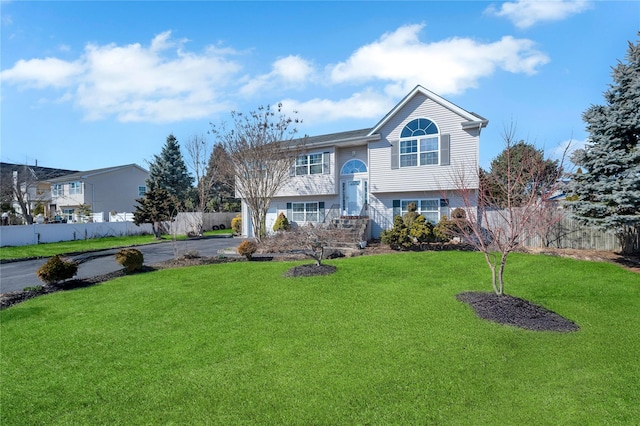 raised ranch featuring aphalt driveway, fence, and a front lawn