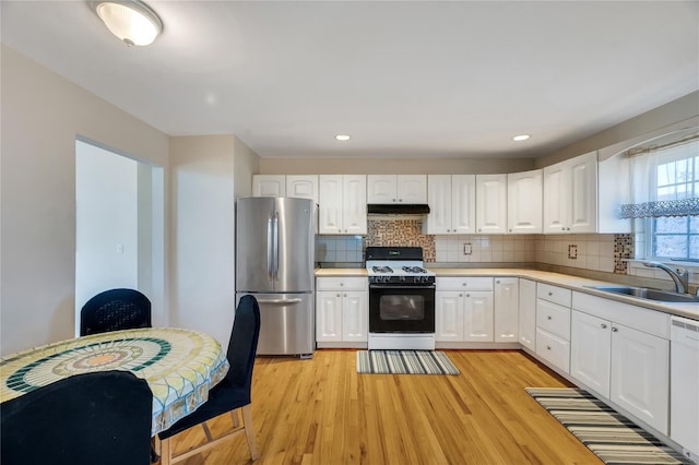 kitchen featuring freestanding refrigerator, a sink, under cabinet range hood, gas range, and light wood-type flooring