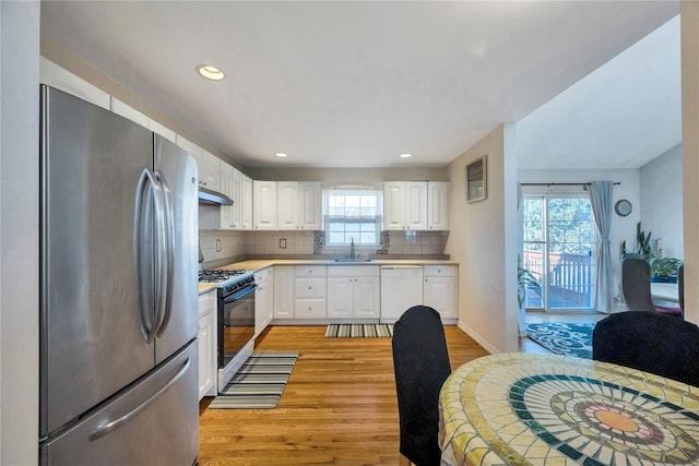 kitchen with white dishwasher, freestanding refrigerator, a sink, under cabinet range hood, and gas range