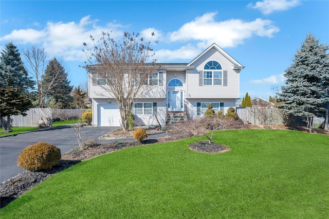 bi-level home with aphalt driveway, an attached garage, fence, and a front yard