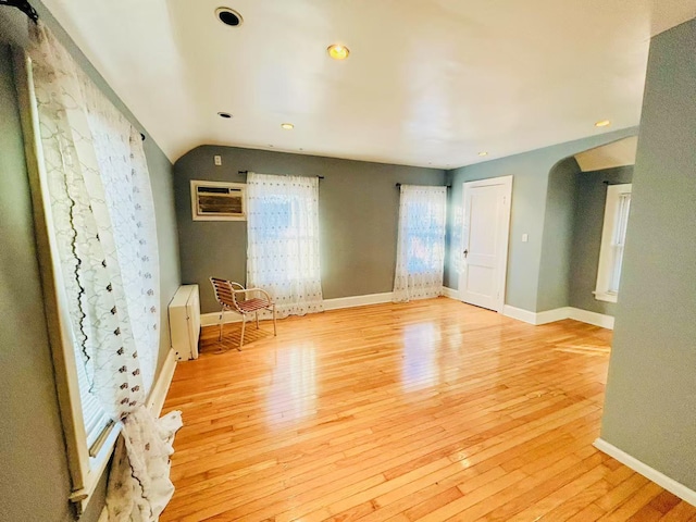 unfurnished room with lofted ceiling, light wood-style flooring, baseboards, and arched walkways