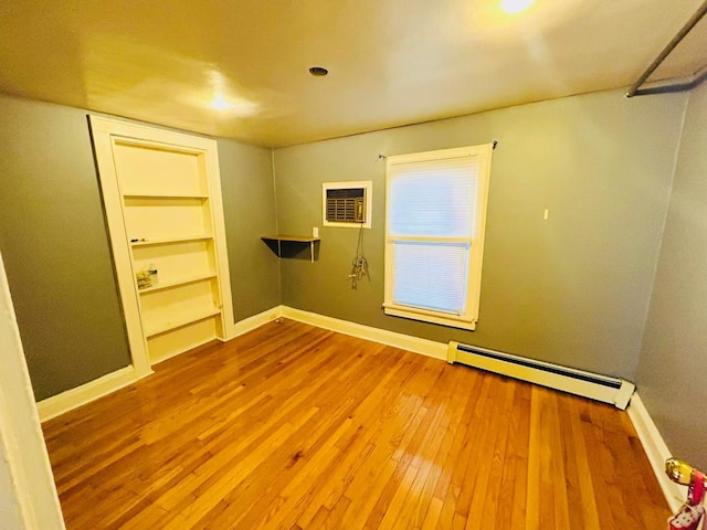 empty room featuring a baseboard heating unit, wood-type flooring, baseboards, and built in shelves