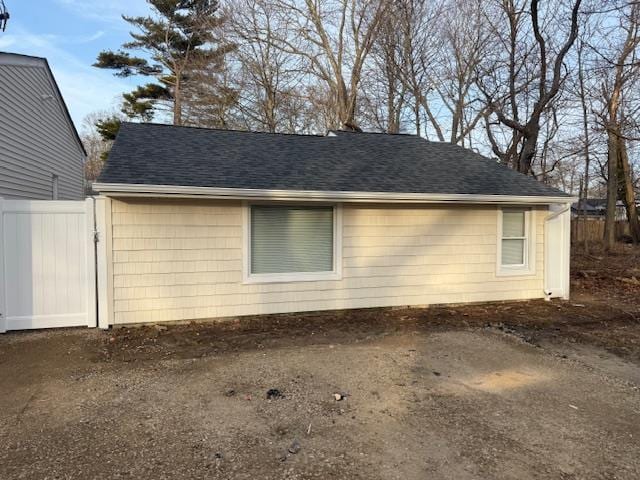 view of side of property with a shingled roof and fence