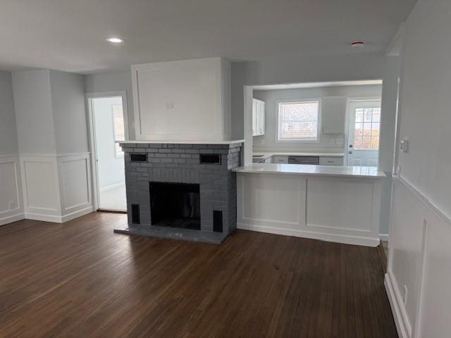 unfurnished living room with recessed lighting, wainscoting, a decorative wall, a brick fireplace, and dark wood-style flooring