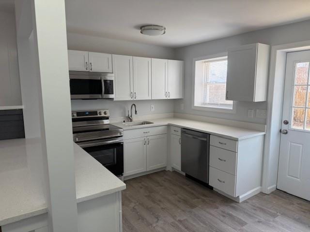 kitchen with light wood-style flooring, a sink, stainless steel appliances, light countertops, and white cabinets