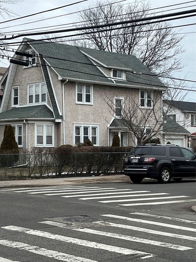 multi unit property featuring roof with shingles, a gambrel roof, a fenced front yard, and stucco siding