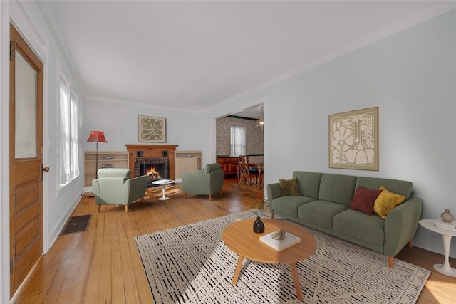 living area featuring a brick fireplace, plenty of natural light, light wood-style floors, and ornamental molding