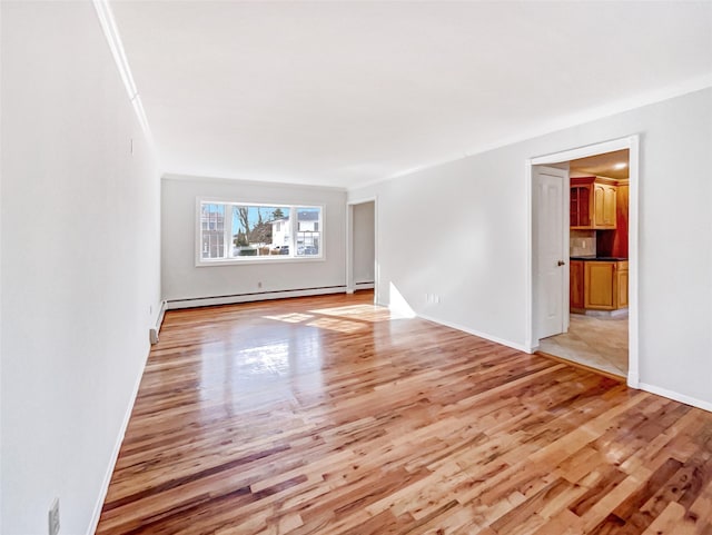 spare room featuring light wood finished floors, a baseboard heating unit, baseboards, and ornamental molding