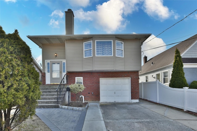 view of front of house with driveway, fence, a garage, brick siding, and a chimney