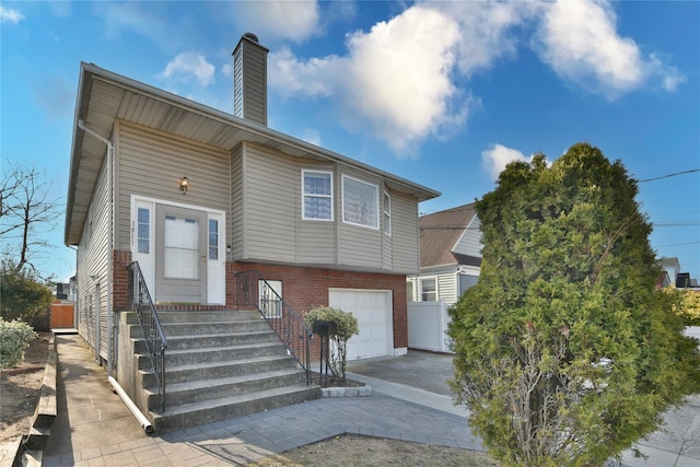 view of front facade with driveway, brick siding, an attached garage, and a chimney