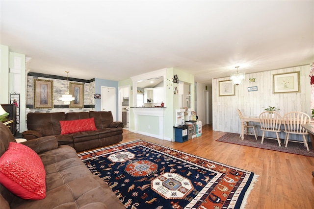 living room featuring a notable chandelier, an accent wall, baseboards, and wood finished floors