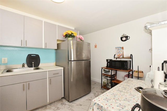 kitchen featuring black microwave, light countertops, freestanding refrigerator, marble finish floor, and a sink